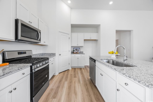 kitchen featuring a sink, light wood-style floors, white cabinetry, light stone countertops, and appliances with stainless steel finishes