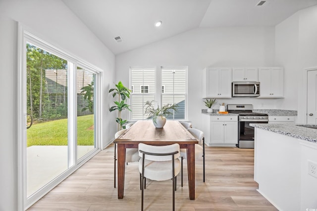 kitchen with white cabinets, stainless steel appliances, light stone countertops, light wood-style flooring, and high vaulted ceiling