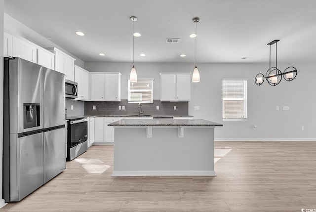 kitchen with light stone countertops, a center island, decorative light fixtures, white cabinets, and appliances with stainless steel finishes