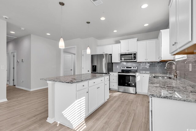 kitchen featuring appliances with stainless steel finishes, hanging light fixtures, a center island, white cabinets, and sink