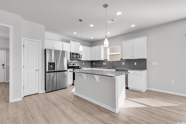 kitchen with hanging light fixtures, a kitchen island, white cabinetry, appliances with stainless steel finishes, and dark stone countertops