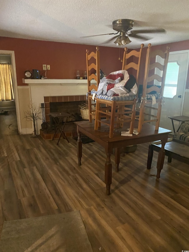 dining space featuring a fireplace, a textured ceiling, ceiling fan, and dark wood-type flooring