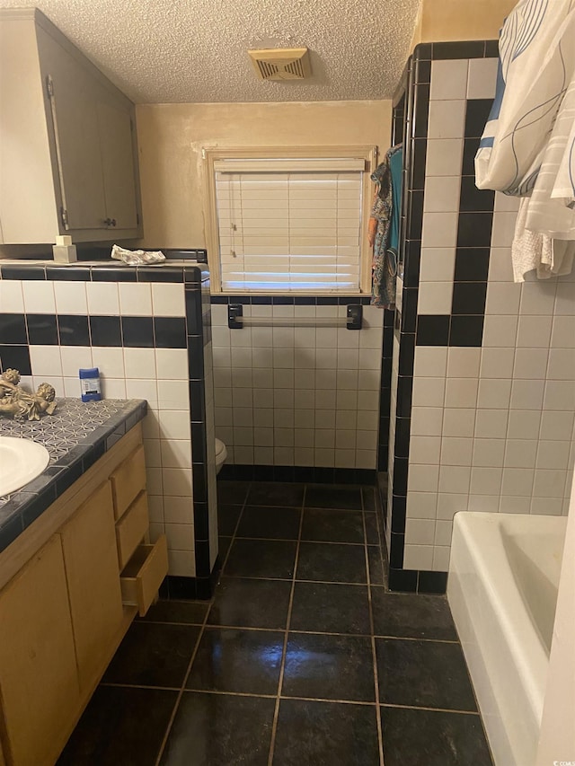 bathroom featuring a textured ceiling, tile patterned floors, vanity, and tile walls