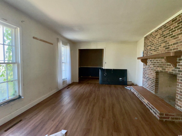 unfurnished living room with dark wood-type flooring and a brick fireplace