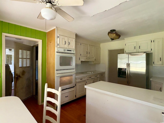 kitchen with double oven, dark wood-type flooring, stainless steel refrigerator with ice dispenser, crown molding, and ceiling fan