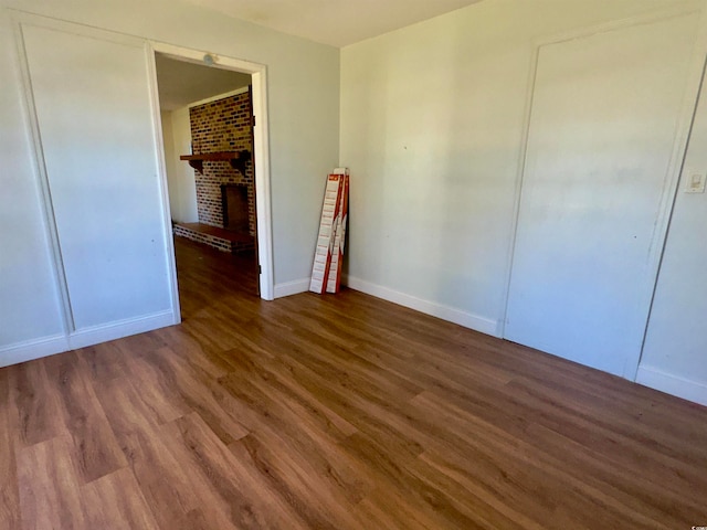 unfurnished bedroom featuring dark hardwood / wood-style flooring and a brick fireplace