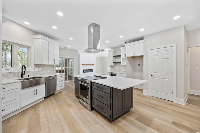 kitchen with appliances with stainless steel finishes, white cabinetry, sink, and island range hood