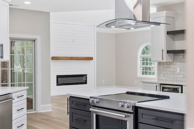 kitchen featuring appliances with stainless steel finishes, light wood-type flooring, a fireplace, island exhaust hood, and white cabinetry