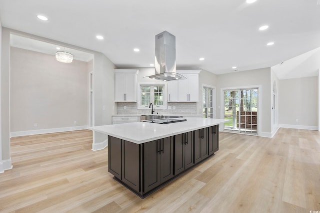 kitchen with island exhaust hood, decorative backsplash, light wood-type flooring, and white cabinets