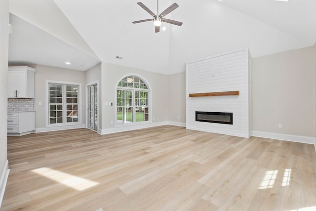 unfurnished living room featuring light hardwood / wood-style flooring, high vaulted ceiling, a large fireplace, and ceiling fan