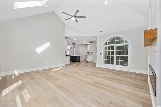 unfurnished living room featuring a large fireplace, a skylight, high vaulted ceiling, light hardwood / wood-style floors, and ceiling fan