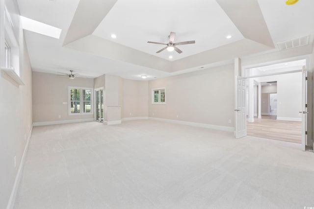 spare room featuring light colored carpet, a tray ceiling, a skylight, and ceiling fan