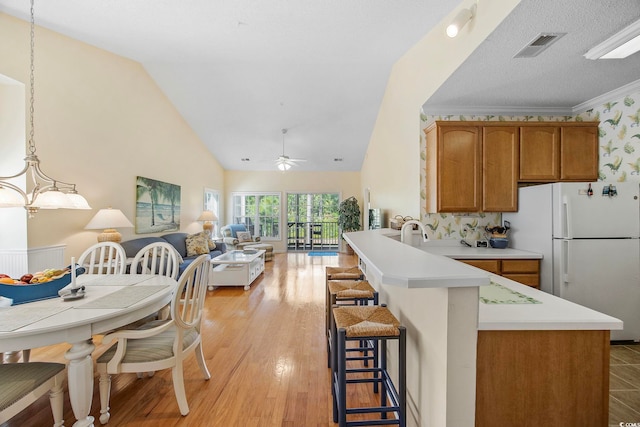 kitchen with lofted ceiling, ceiling fan with notable chandelier, light hardwood / wood-style floors, decorative light fixtures, and white fridge