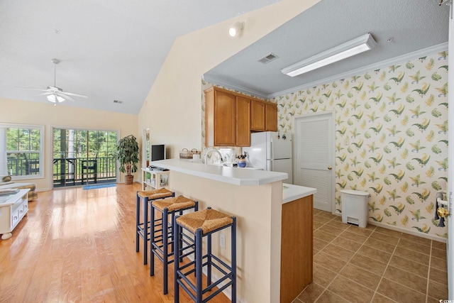 kitchen with vaulted ceiling, ornamental molding, kitchen peninsula, and white fridge