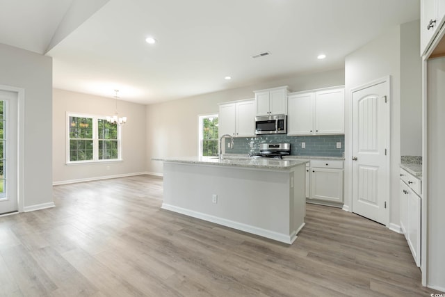 kitchen with white cabinetry, appliances with stainless steel finishes, a kitchen island with sink, vaulted ceiling, and a chandelier