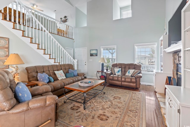 living room with ceiling fan, hardwood / wood-style flooring, a stone fireplace, and a towering ceiling