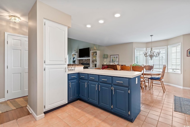 kitchen with kitchen peninsula, light tile patterned floors, decorative light fixtures, blue cabinetry, and a stone fireplace