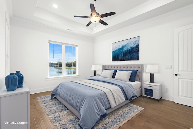 bedroom featuring ceiling fan, a tray ceiling, dark hardwood / wood-style flooring, ornamental molding, and a water view