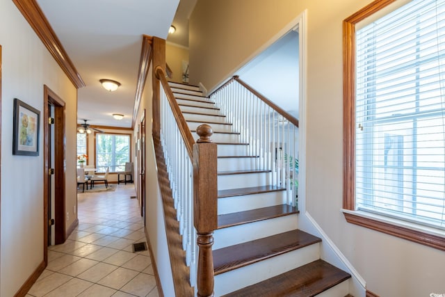 stairs featuring ceiling fan, a healthy amount of sunlight, ornamental molding, and tile patterned flooring