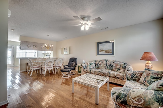 living room with light hardwood / wood-style flooring, a textured ceiling, and ceiling fan with notable chandelier