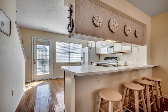 kitchen featuring white appliances, light wood-type flooring, a textured ceiling, kitchen peninsula, and a breakfast bar