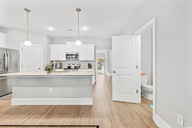 kitchen featuring appliances with stainless steel finishes, light wood-type flooring, white cabinetry, decorative light fixtures, and light stone counters