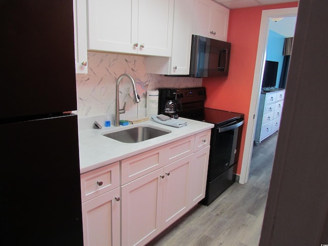 kitchen with white cabinets, decorative backsplash, black appliances, sink, and light hardwood / wood-style flooring