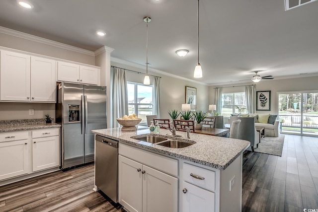 kitchen featuring sink, appliances with stainless steel finishes, white cabinetry, a center island with sink, and decorative light fixtures