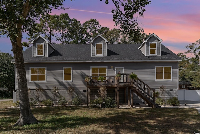 back house at dusk featuring a deck and a lawn