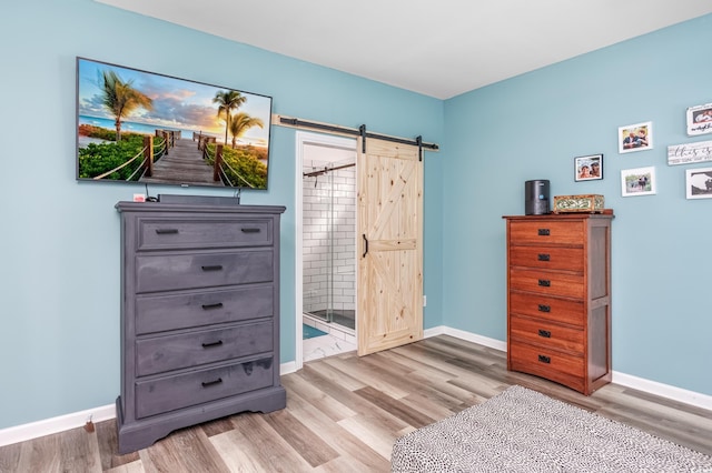 bedroom featuring ensuite bathroom, light hardwood / wood-style flooring, and a barn door