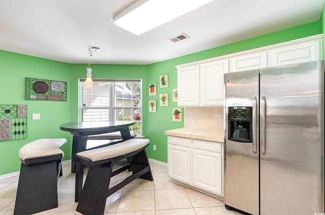 kitchen featuring tile countertops, pendant lighting, stainless steel fridge, light tile patterned floors, and white cabinetry