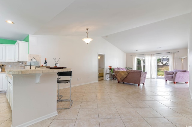 kitchen featuring a breakfast bar area, white cabinetry, light tile patterned floors, and lofted ceiling