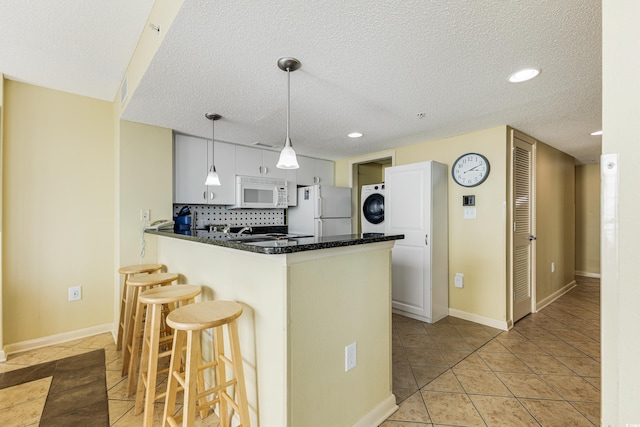 kitchen featuring hanging light fixtures, kitchen peninsula, backsplash, a textured ceiling, and white appliances