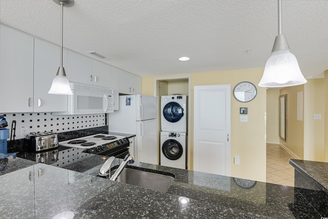 kitchen with white appliances, white cabinetry, dark stone counters, pendant lighting, and stacked washer / drying machine