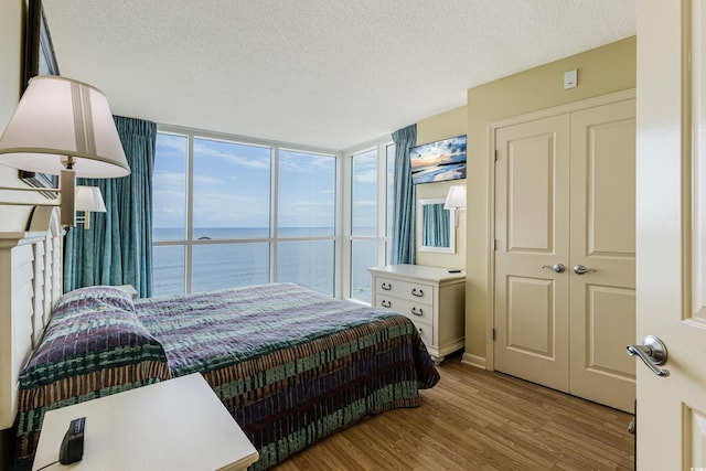 bedroom with a textured ceiling, a closet, light hardwood / wood-style floors, expansive windows, and a water view