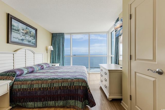 bedroom with a textured ceiling, a water view, light wood-type flooring, and floor to ceiling windows