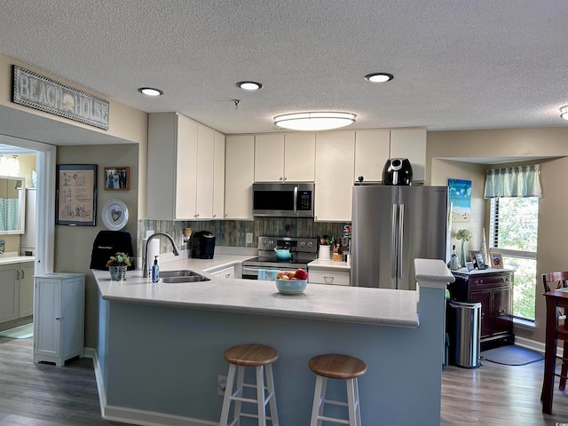 kitchen with kitchen peninsula, stainless steel appliances, wood-type flooring, sink, and white cabinets