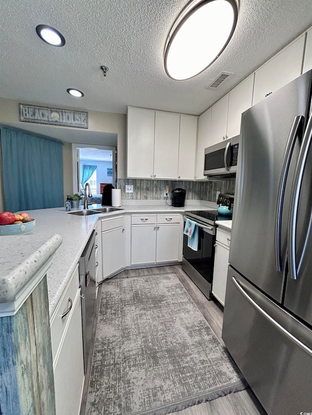 kitchen with appliances with stainless steel finishes, light hardwood / wood-style flooring, white cabinets, and sink