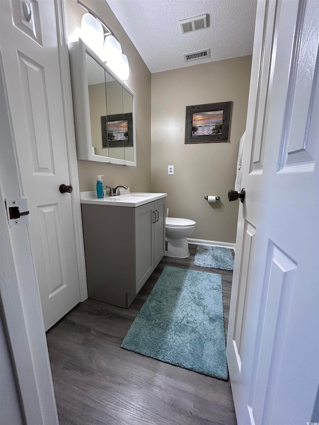 bathroom featuring vanity, a textured ceiling, hardwood / wood-style flooring, and toilet