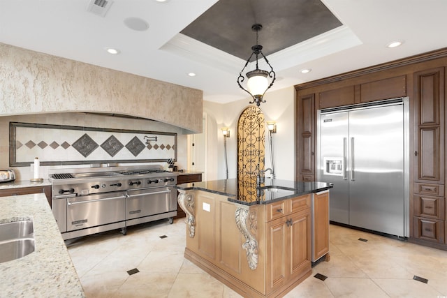 kitchen with a raised ceiling, dark stone counters, high end appliances, and hanging light fixtures