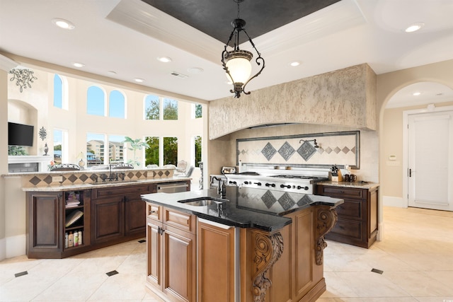 kitchen with backsplash, a raised ceiling, a kitchen island with sink, dark stone counters, and sink