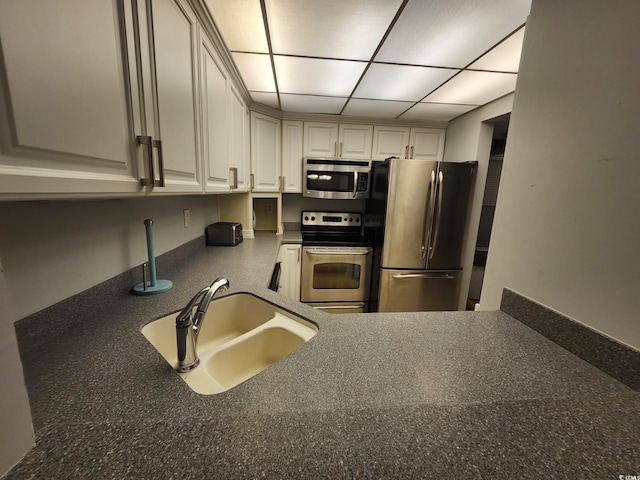 kitchen with appliances with stainless steel finishes, a paneled ceiling, sink, and white cabinetry