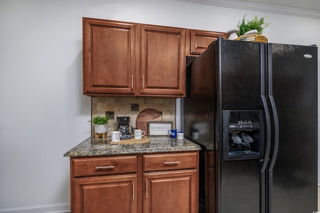 kitchen featuring dark stone countertops, backsplash, ornamental molding, and black fridge