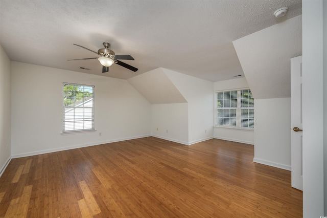 additional living space featuring lofted ceiling, a textured ceiling, hardwood / wood-style flooring, and ceiling fan