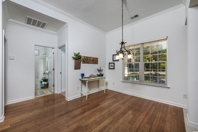 unfurnished dining area featuring a textured ceiling, dark hardwood / wood-style flooring, a chandelier, and ornamental molding