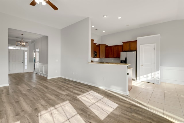 unfurnished living room with ceiling fan with notable chandelier, crown molding, and light hardwood / wood-style flooring