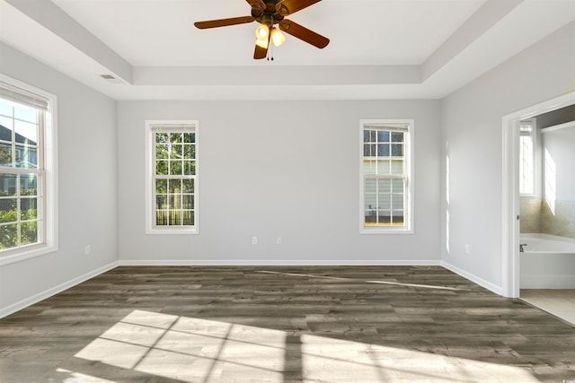 unfurnished room featuring dark wood-type flooring, ceiling fan, plenty of natural light, and a raised ceiling