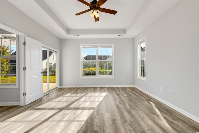 spare room with light wood-type flooring, ceiling fan, and a tray ceiling