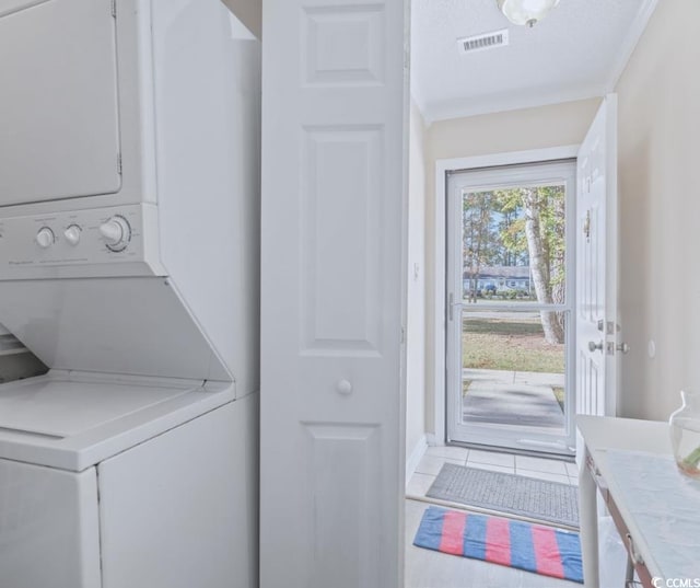 clothes washing area with ornamental molding, stacked washer and dryer, and tile patterned floors