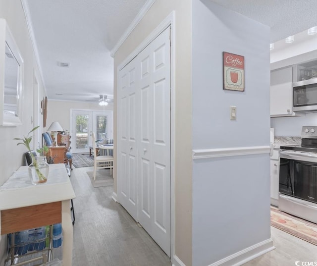 interior space with light wood-type flooring, french doors, crown molding, and a textured ceiling